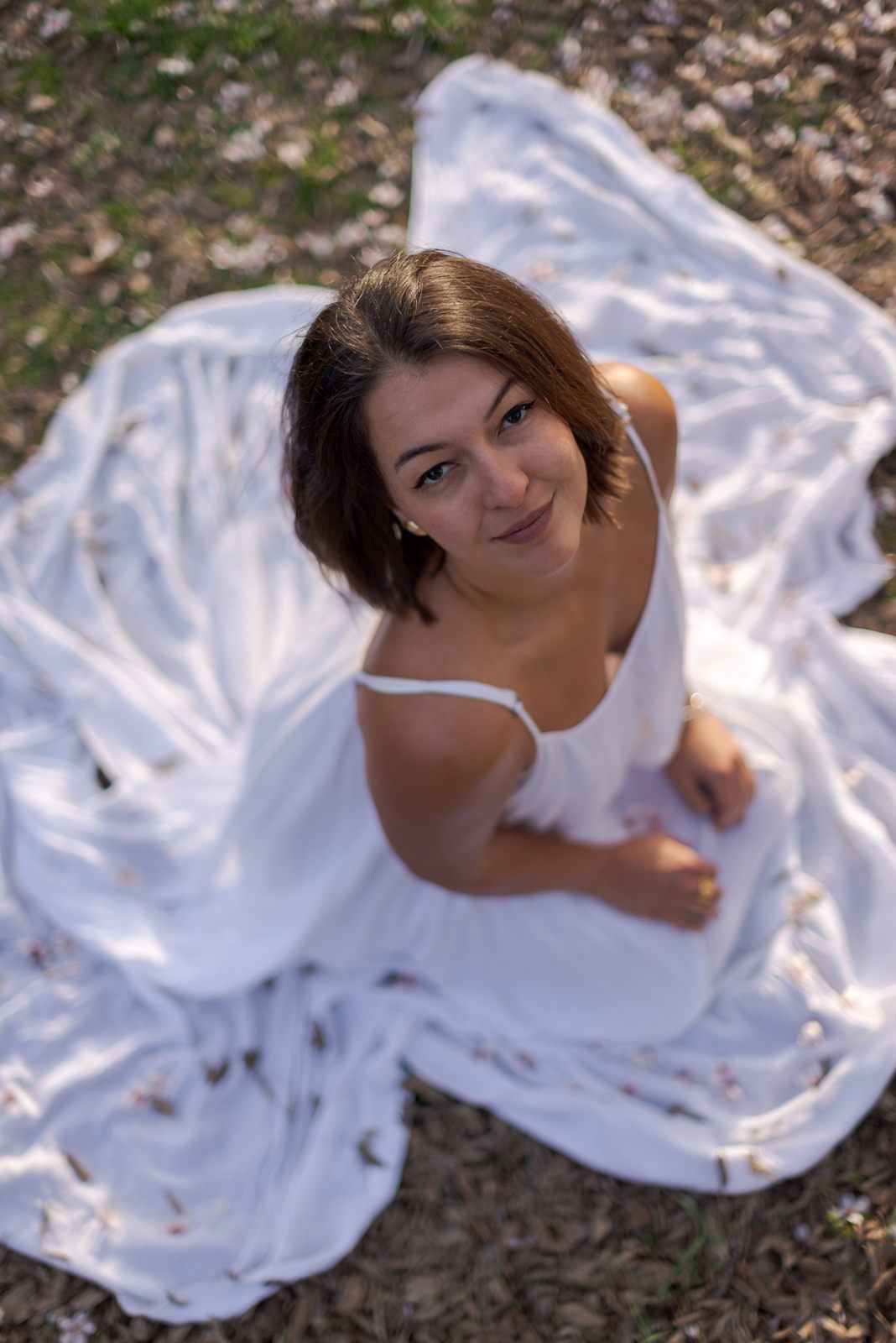 Retrato cenital de una mujer sentada sobre la falda extendida de su vestido blanco.